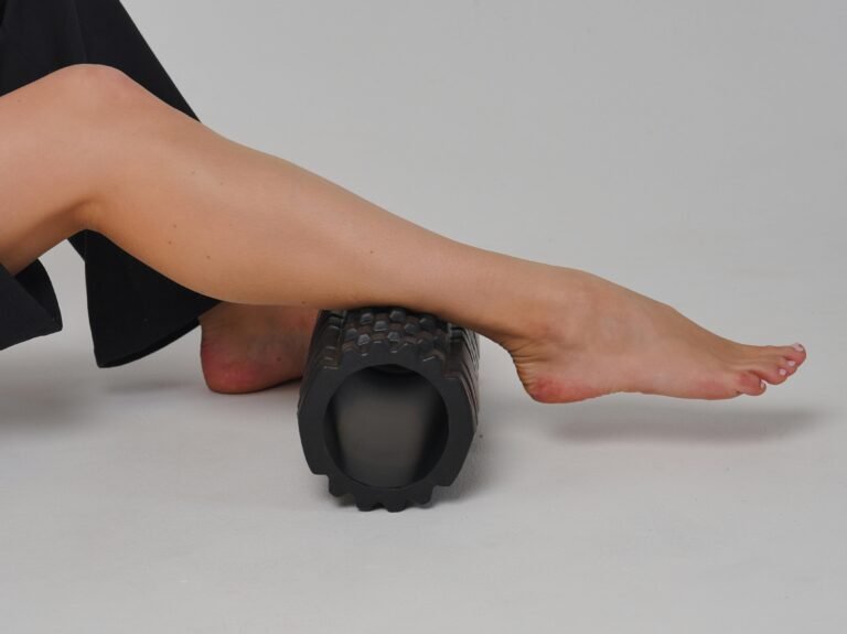 Close-up of a leg using a foam roller for stretching and muscle relief in a studio setting.